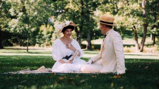 Historiallisiin asuihin pukeutunut pariskunta piknikillä. 